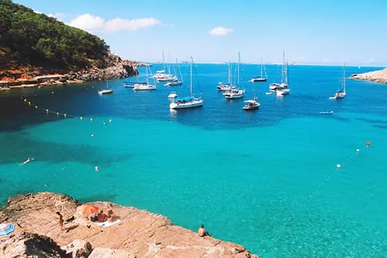 Voiliers au mouillage dans une baie turquoise bordée d’une côte rocheuse.